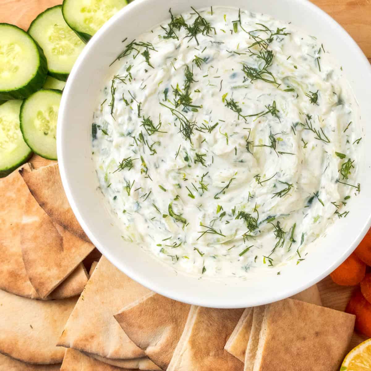 tzatziki sauce in a bowl with and on a platter with vegetables and topped with fresh dill