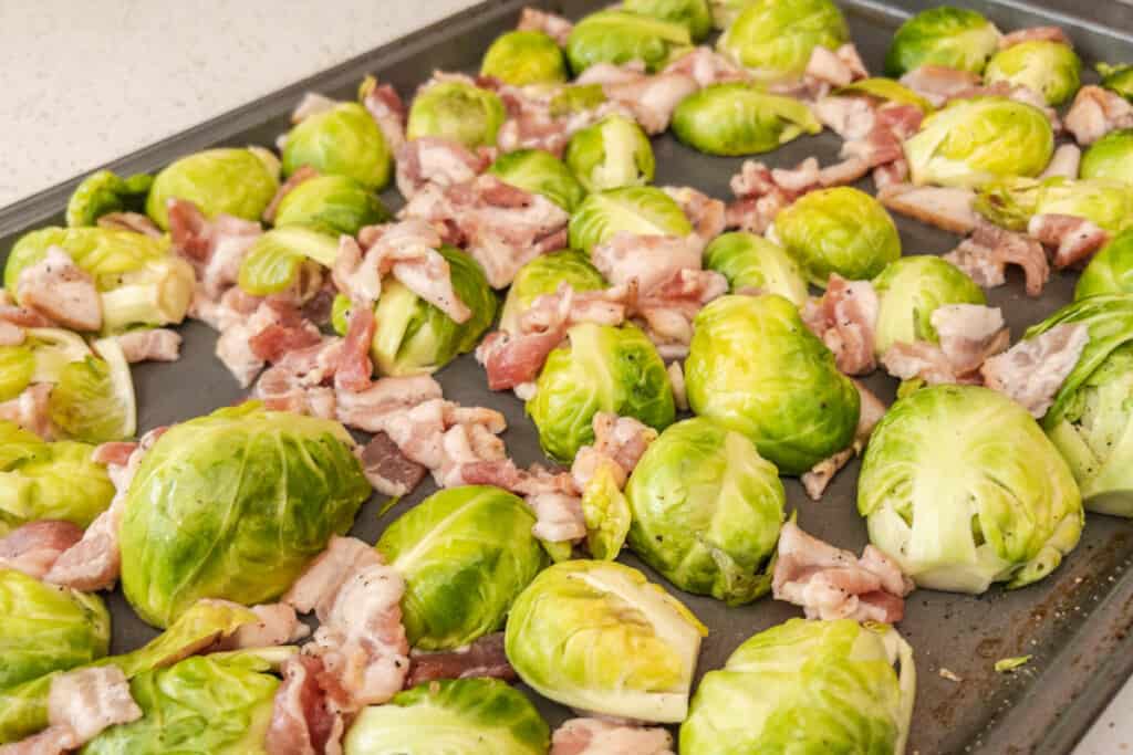 trimmed and halved brussel sprouts in sheet pan with bacon
