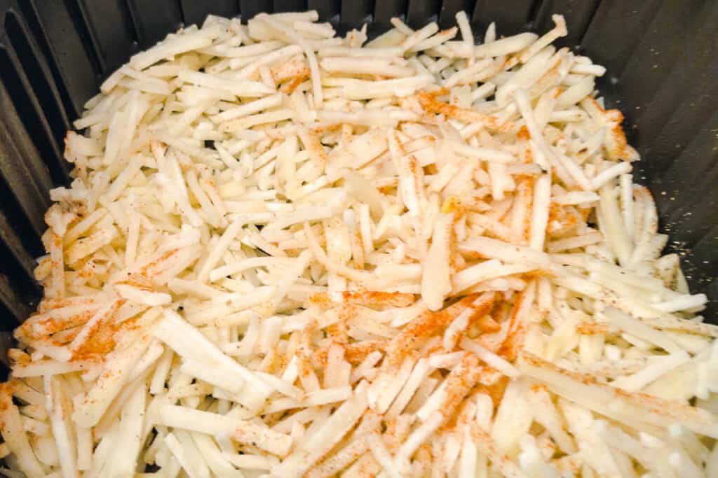 Frozen hash browns in air fryer basket seasoned up and ready to cook.