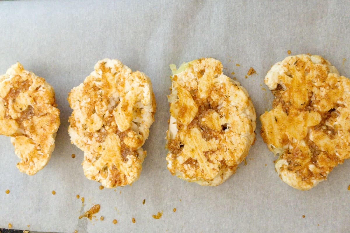 cauliflower steaks brushed with oil and spices and ready to be roasted.