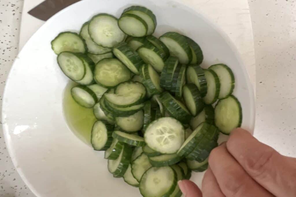 Cucumbers in a bowl with salt and sugar with extracted water on bottom of bowl.