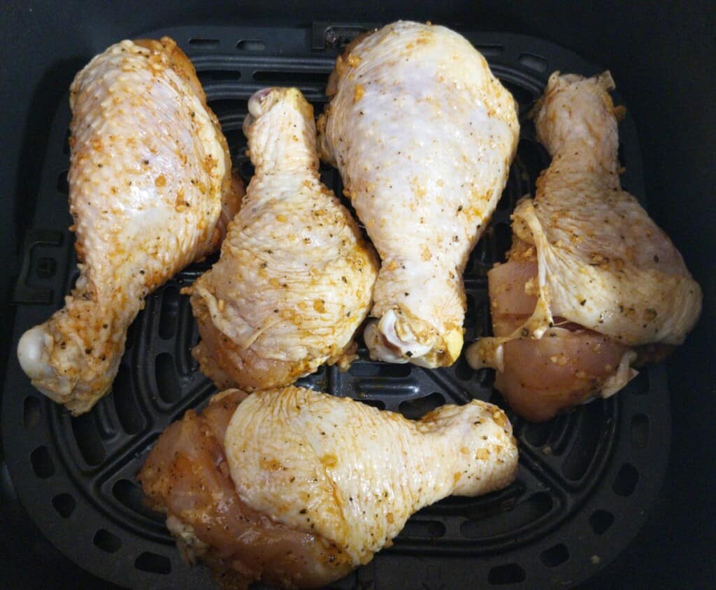 black pepper and garlic chicken legs raw in the air fryer basket ready to be cooked.