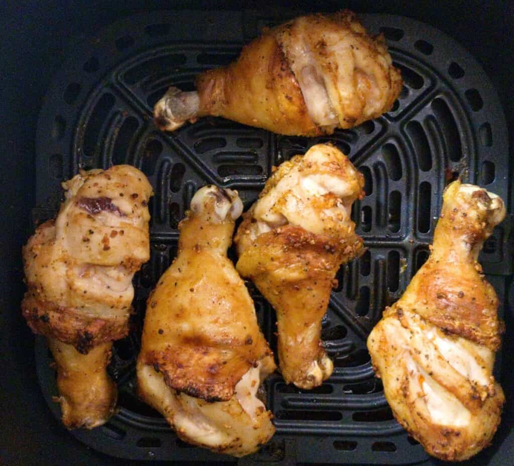 black pepper garlic chicken legs in air fryer basket ready to flip