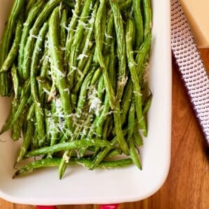 Crispy air fryer green beans topped with grated Parmesan cheese in a white serving dish.