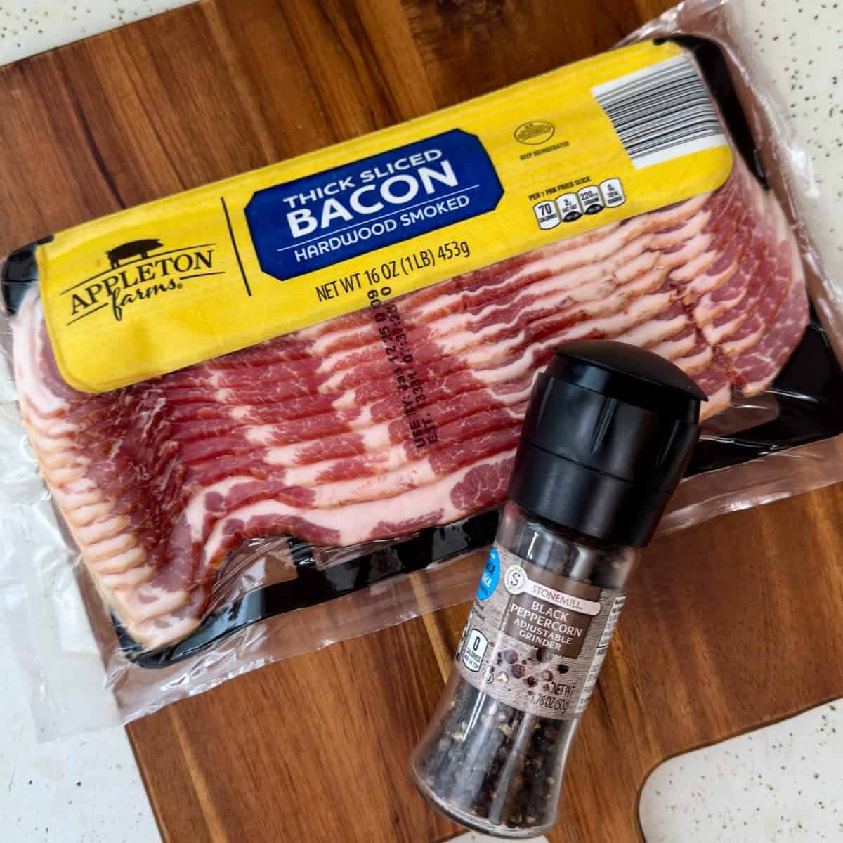 Packaged thick-cut bacon and black pepper grinder on a wooden cutting board, ready for cooking in the air fryer.