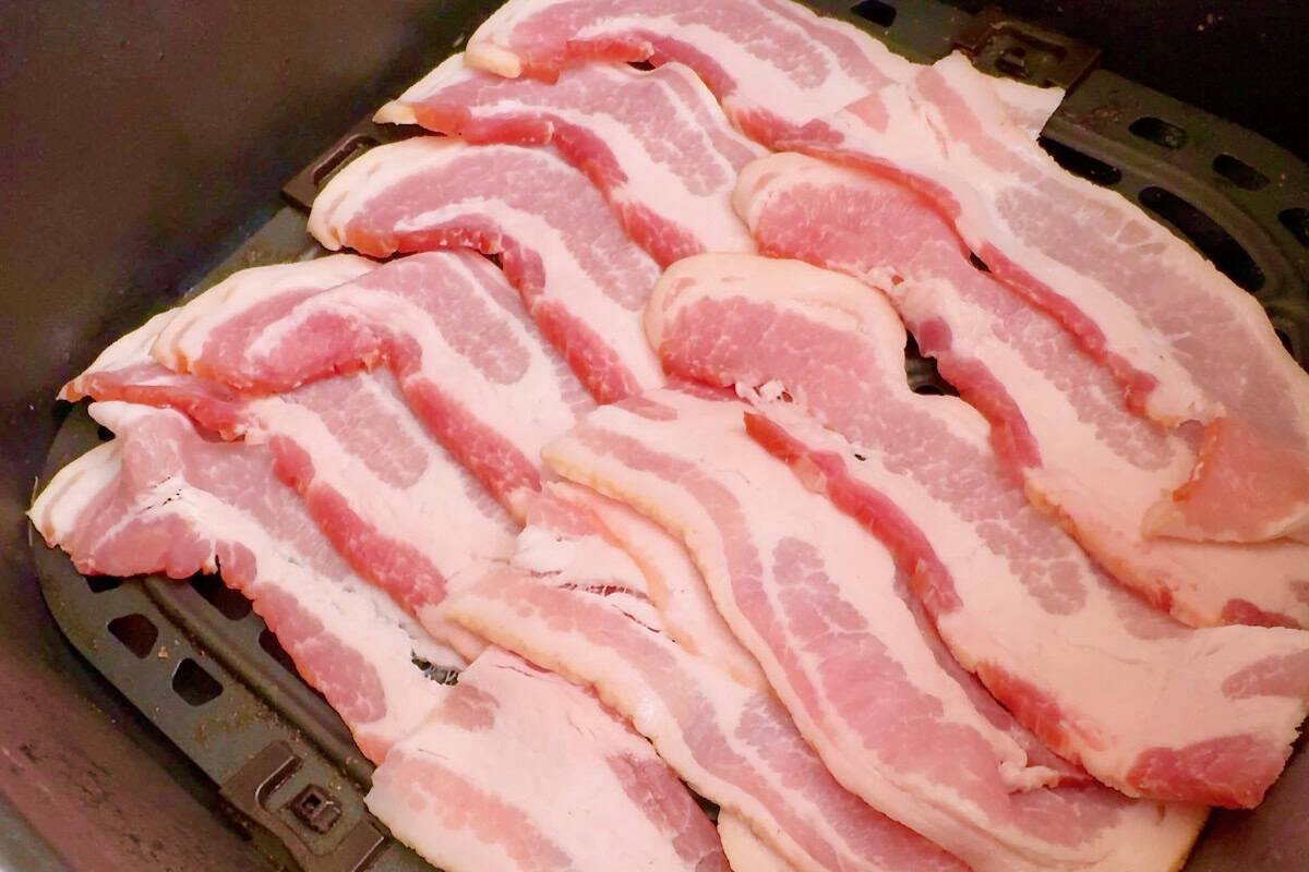 Raw bacon strips arranged in a single layer inside an air fryer basket before cooking.