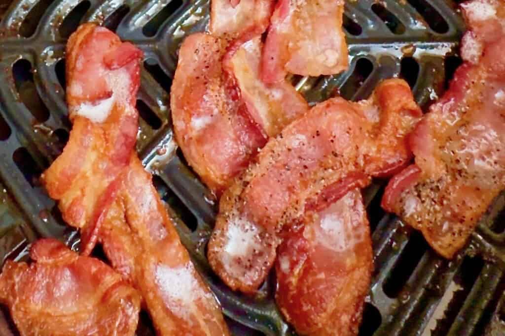 Partially cooked bacon in the air fryer, crispy on one side, ready to be flipped for even cooking.