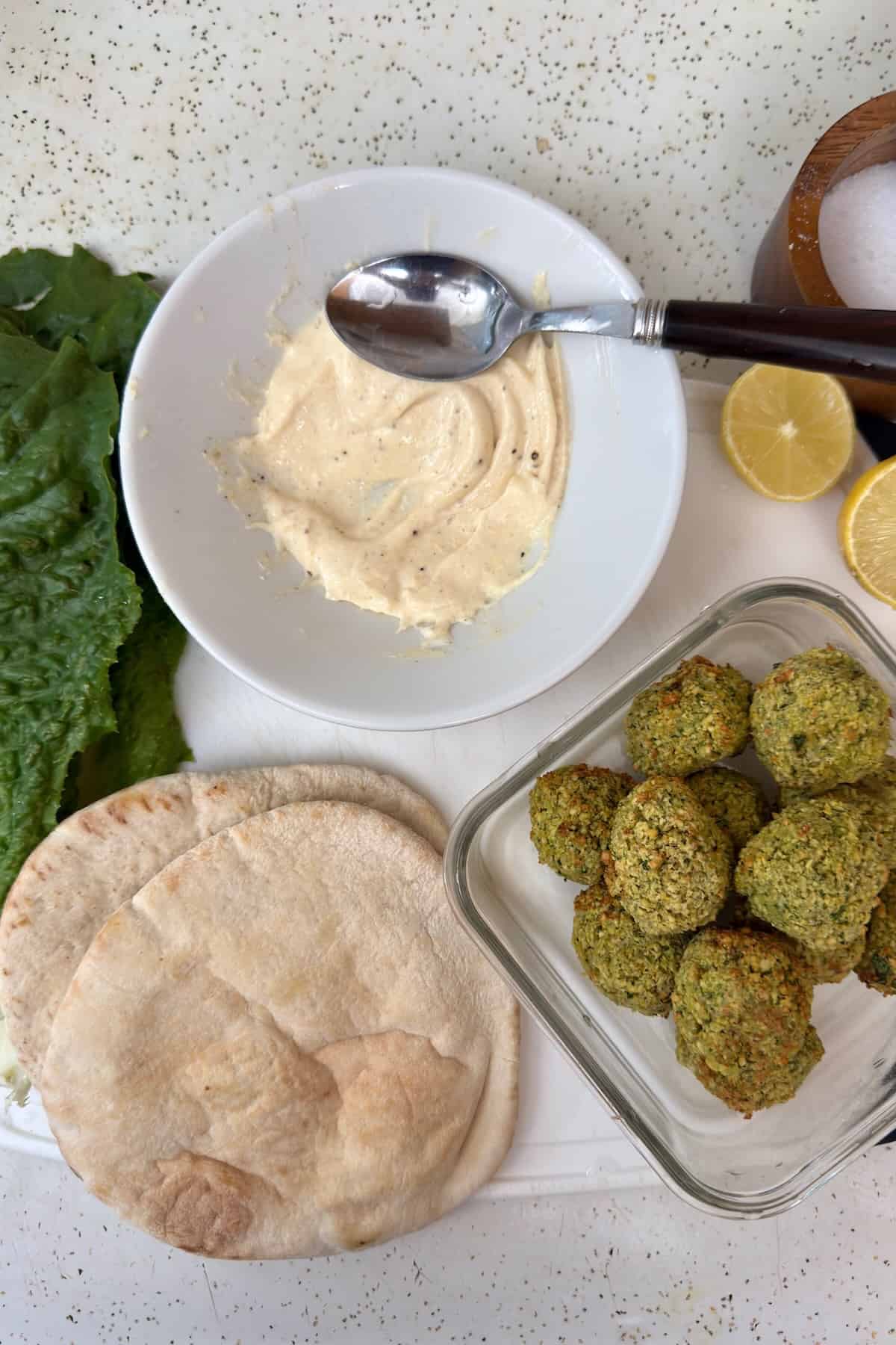 Ingredients for assembling falafel pita, including lettuce, sauce, and fresh falafel.