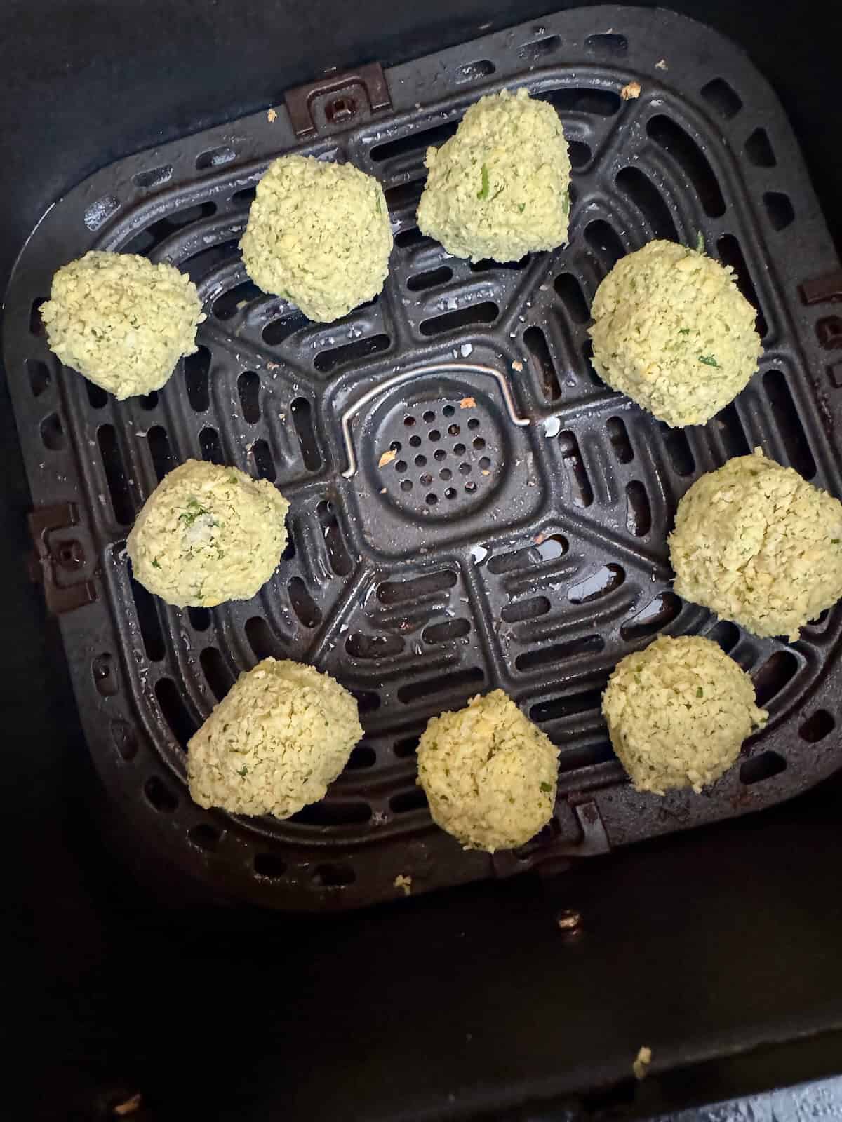Uncooked falafel balls placed in an air fryer basket before cooking.