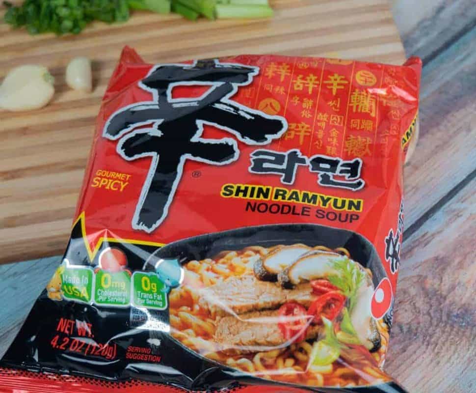 Nongshim Shin Ramyun instant noodles with fresh ingredients on a wooden board.