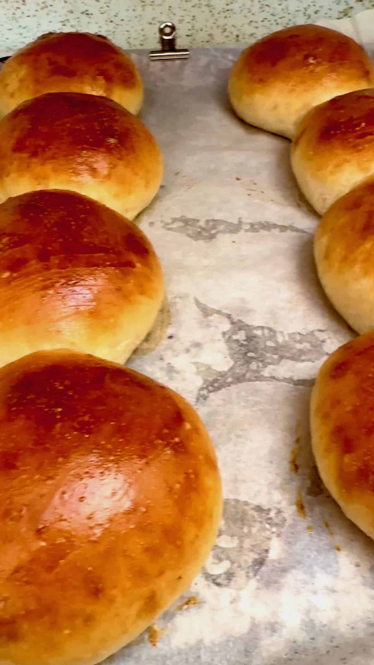 Freshly baked homemade sandwich rolls cooling on a parchment-lined baking sheet