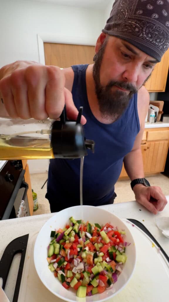Pouring olive oil over the vegetables for Shirazi salad