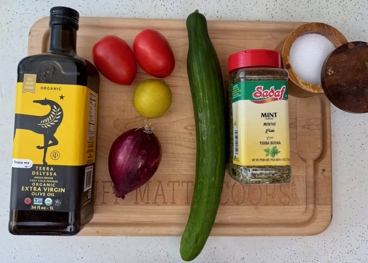 Ingredients for Shirazi salad including cucumbers, tomatoes, red onion, lime, olive oil, dried mint, salt, and black pepper