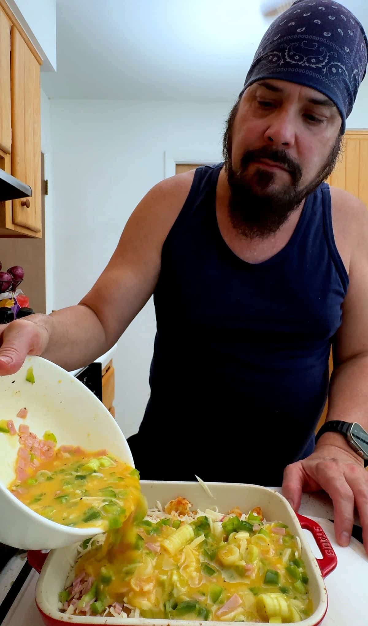 Pouring the egg mixture over the ham, peppers, cheese, and hash brown patties.